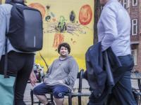 Jonas, som er tidligere hjemløs men i dag studerende, sidder på en bænk og kigger på kameraet, mens folk går forbi