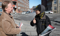 Hus Forbi-sælger på gaden, der taler med en kunde og holder avisen frem