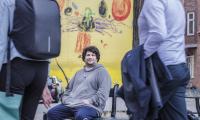 Jonas, som er tidligere hjemløs men i dag studerende, sidder på en bænk og kigger på kameraet, mens folk går forbi