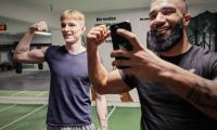 To unge mennesker i et træningscenter spænder overarmen og tager et billede