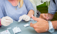 Hænder over et bord, det ene sæt hænder med handsker på er ved at udføre en hepatitis c test